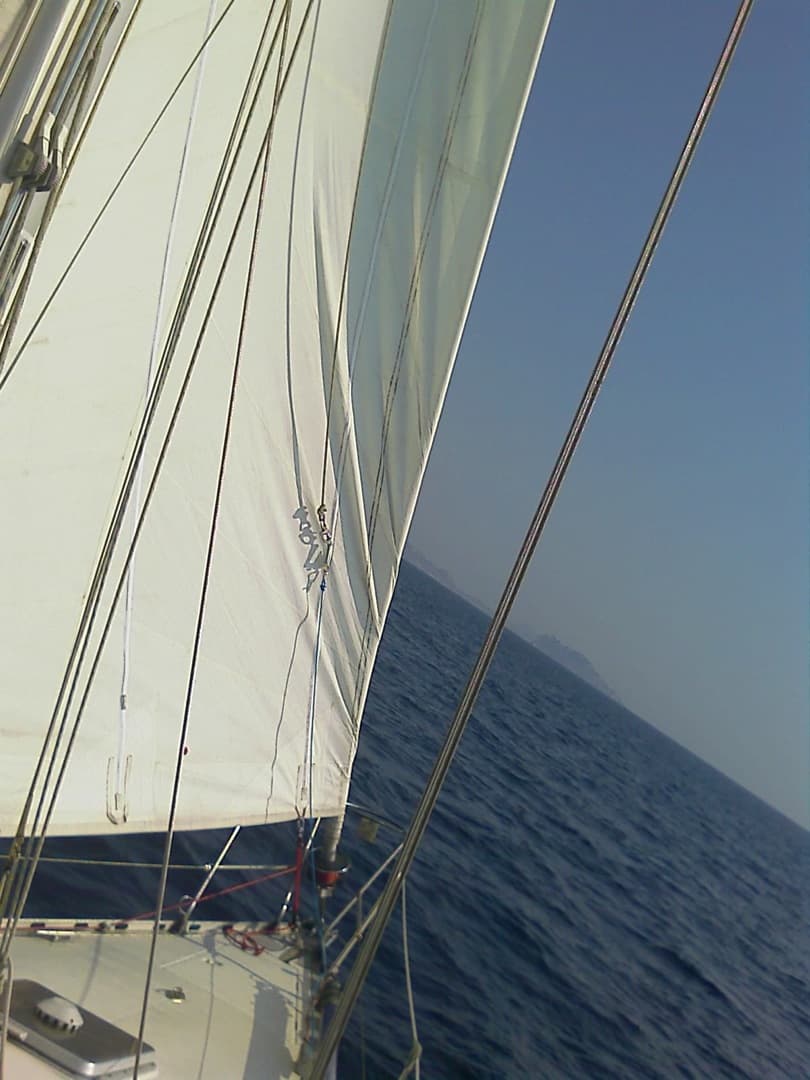 Foc blanc et cordages au-dessus du pont, en navigation sur une mer bleue.